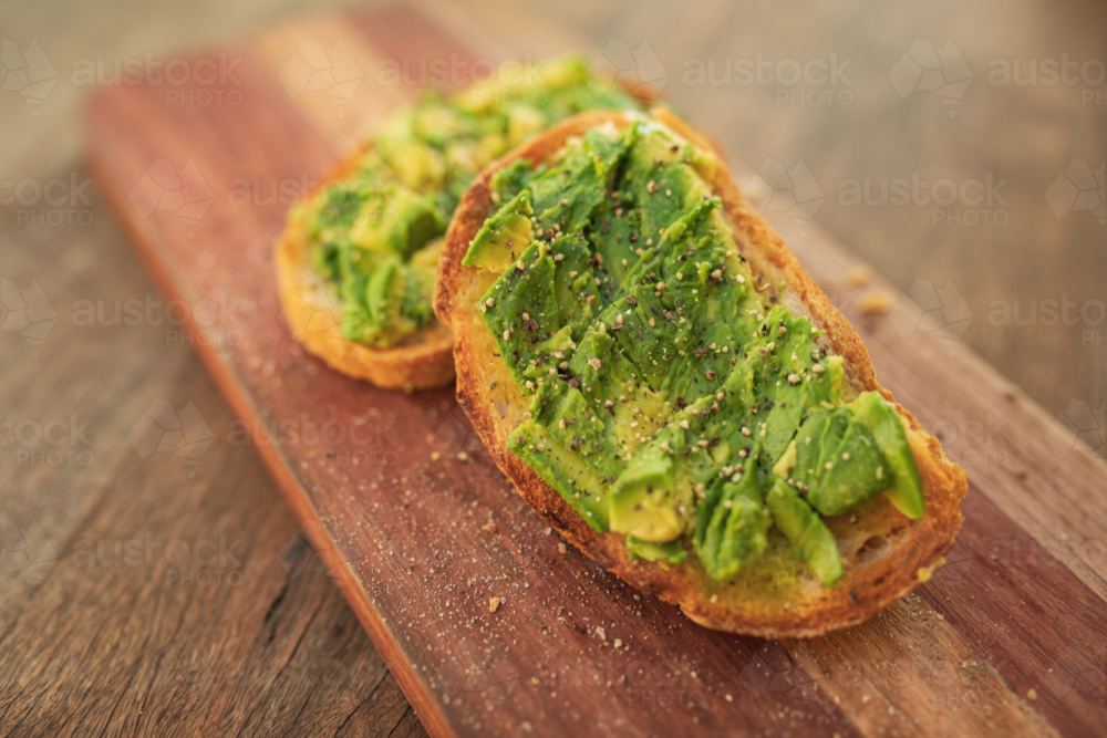 Smashed avocado on toast with salt and pepper on wooden board - Australian Stock Image