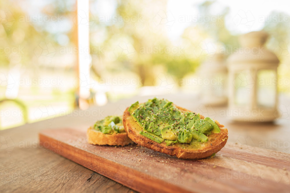Smashed avocado on toast with salt and pepper on wooden board on outdoor table - Australian Stock Image