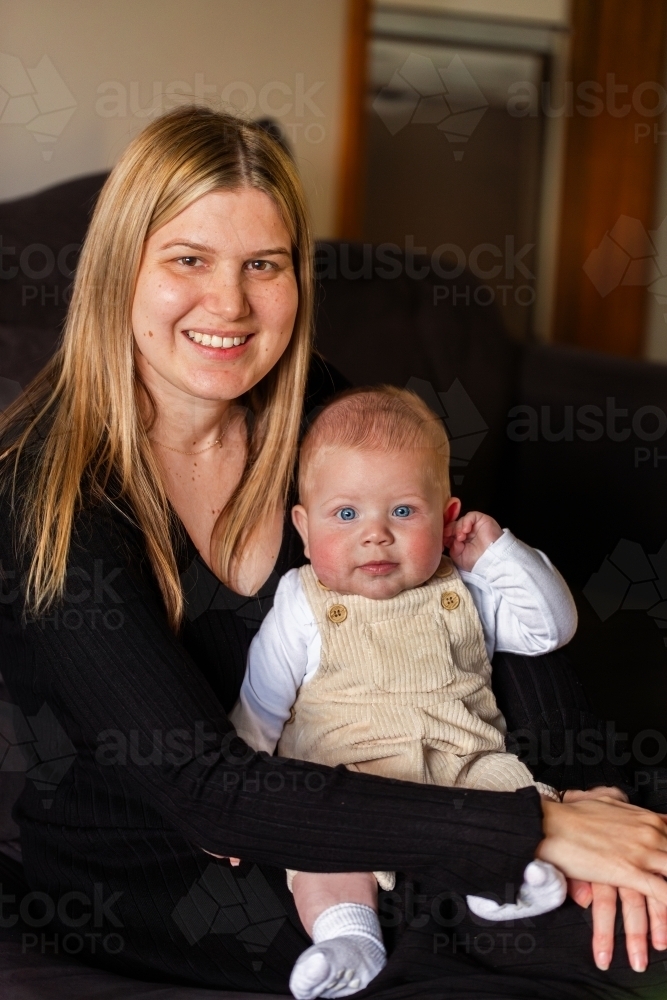 smiling aboriginal mother holding baby boy on lap in home - Australian Stock Image