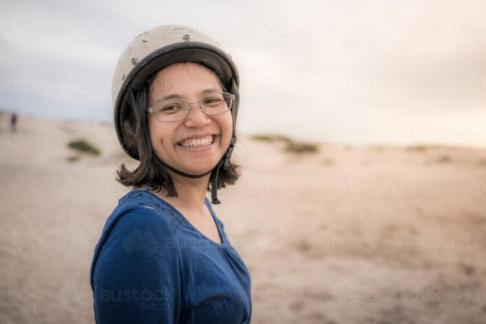 Smiling Asian mother ready to ride camels on beach at sunset - Australian Stock Image