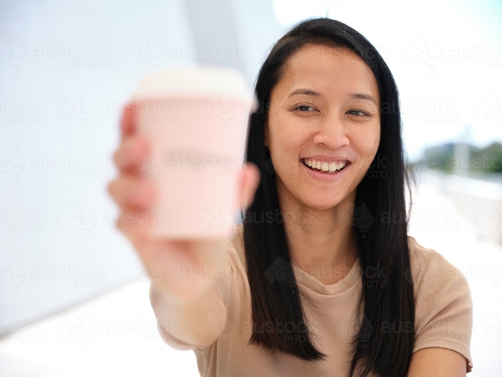 Image of Smiling Asian woman holding out a coffee cup - Austockphoto