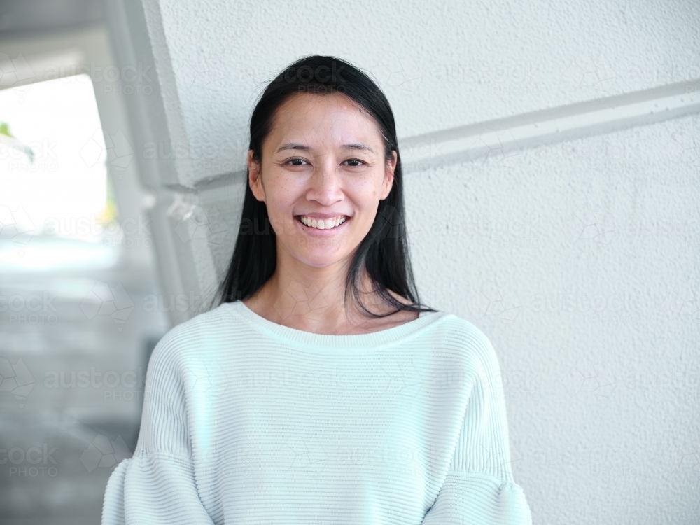 Smiling Asian woman standing in front of a blank wall outside - Australian Stock Image