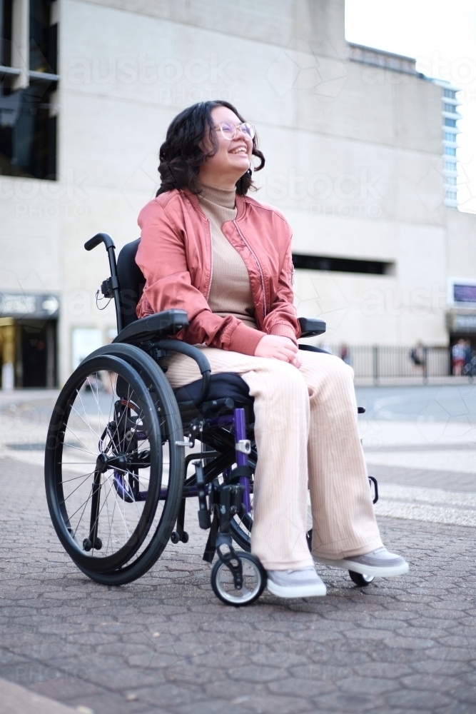 Smiling Asian woman with a disability sitting in a wheelchair outside - Australian Stock Image