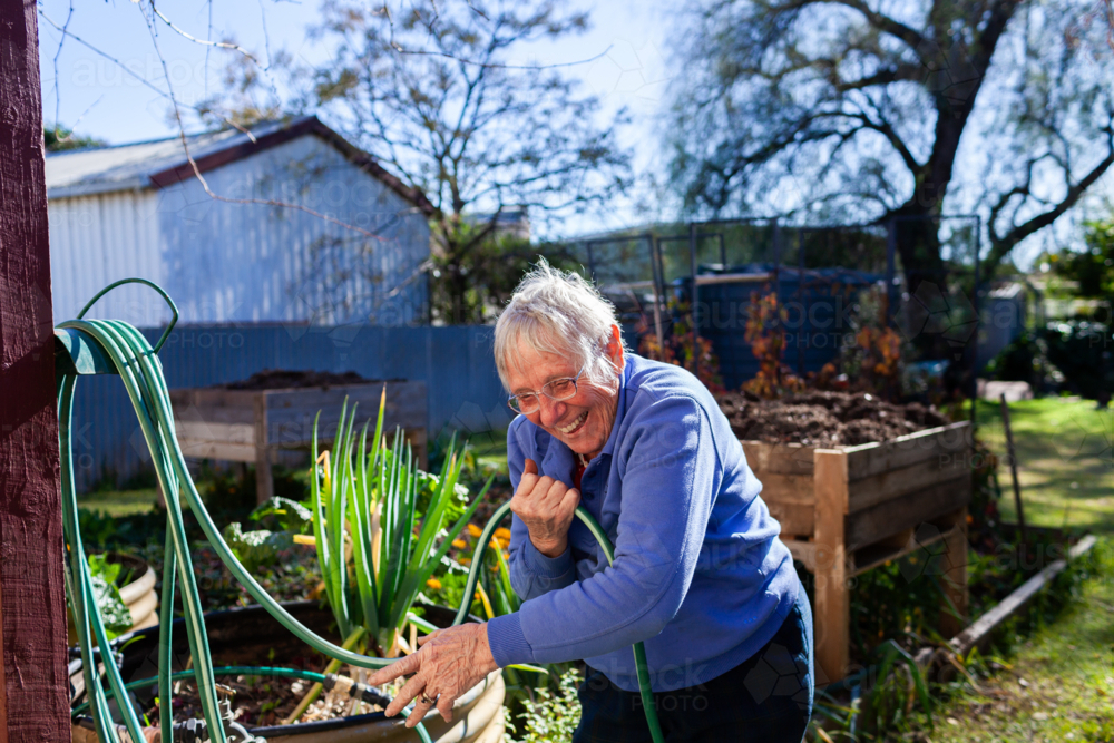 Smiling Aussie woman in her eighties working in garden at home - Australian Stock Image