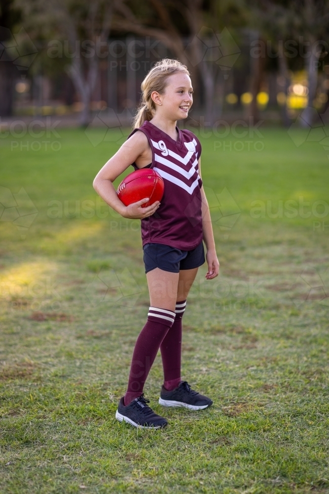 smiling blonde girl standing holding football - Australian Stock Image