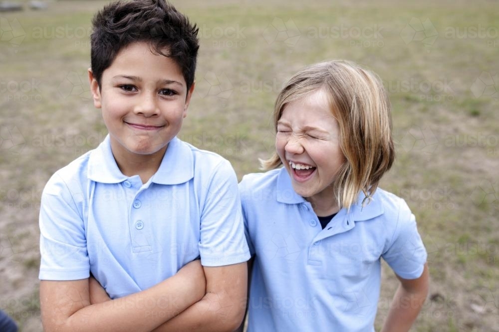 Smiling boy and girl standing outside wearing school unifom - Australian Stock Image