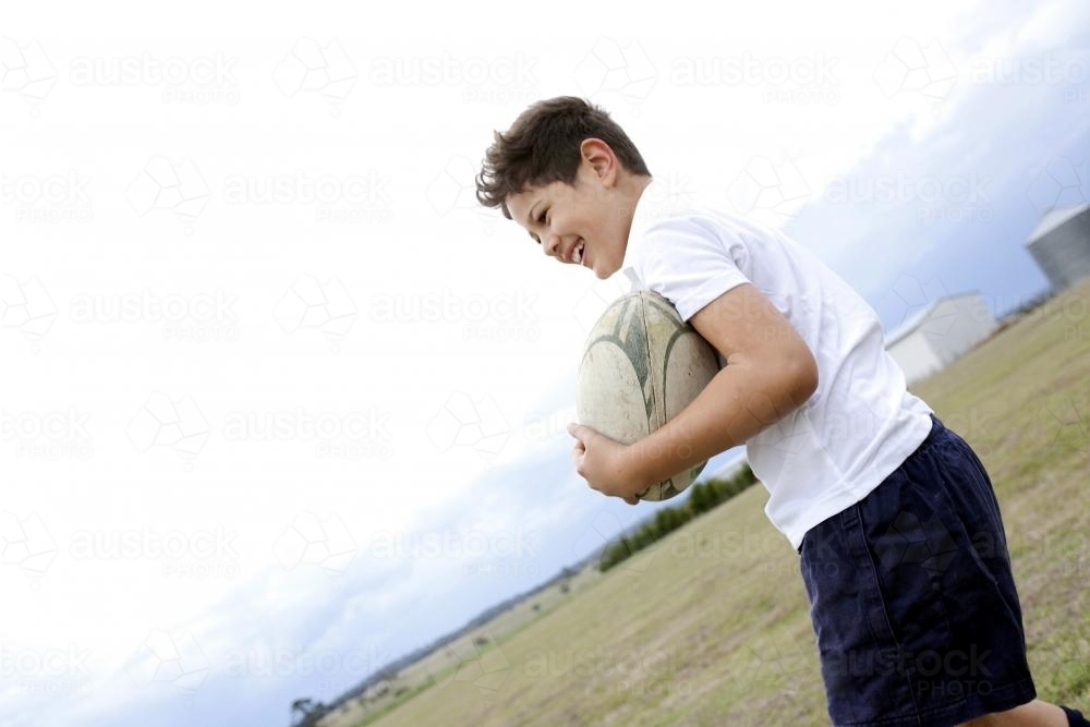 Smiling boy holding a rugby ball on a field - Australian Stock Image