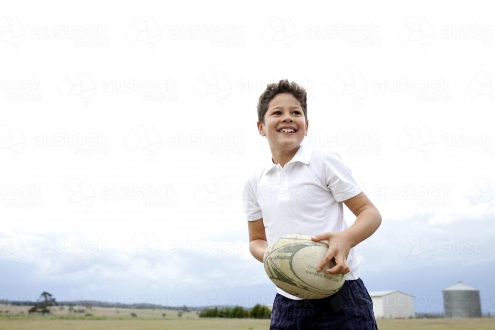 Smiling boy holding footy outside - Australian Stock Image