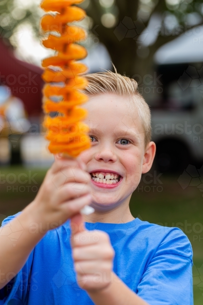 Smiling boy holding up hot chips on a stick – tornado potatoes - Australian Stock Image