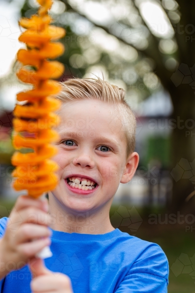 Smiling boy holding up hot chips on a stick – tornado potatoes - Australian Stock Image