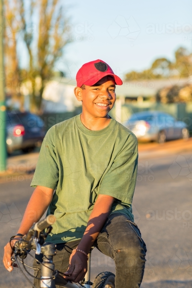 smiling boy looking at camera resting on bike - Australian Stock Image