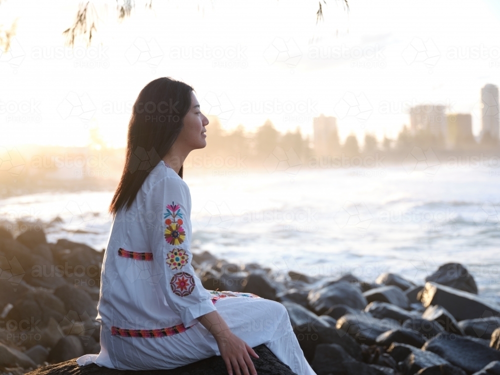 Image of Smiling Chinese woman sitting on rocks by the shore in the ...