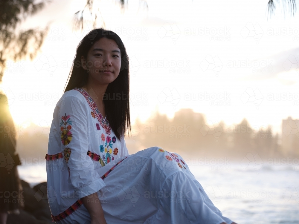 Image of Smiling Chinese woman sitting on rocks by the shore in the ...