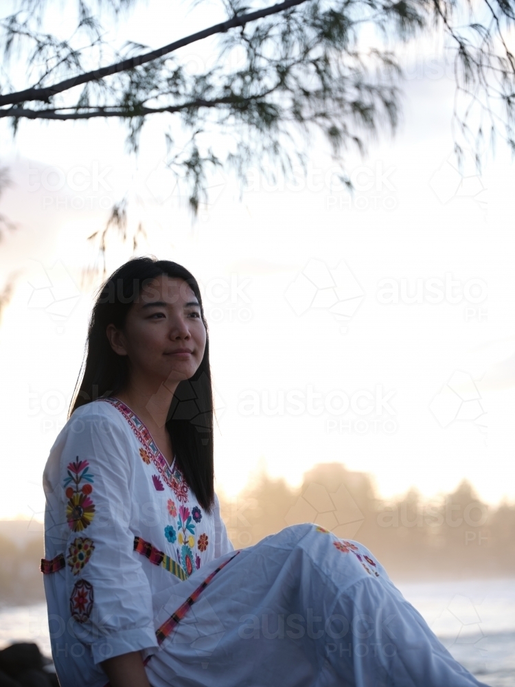 Image of Smiling Chinese woman sitting on rocks by the shore in the ...