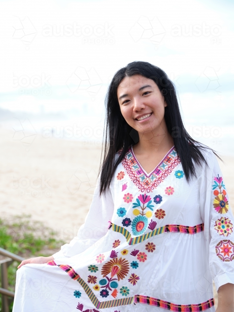 Smiling Chinese woman wearing floral dress at a beach - Australian Stock Image