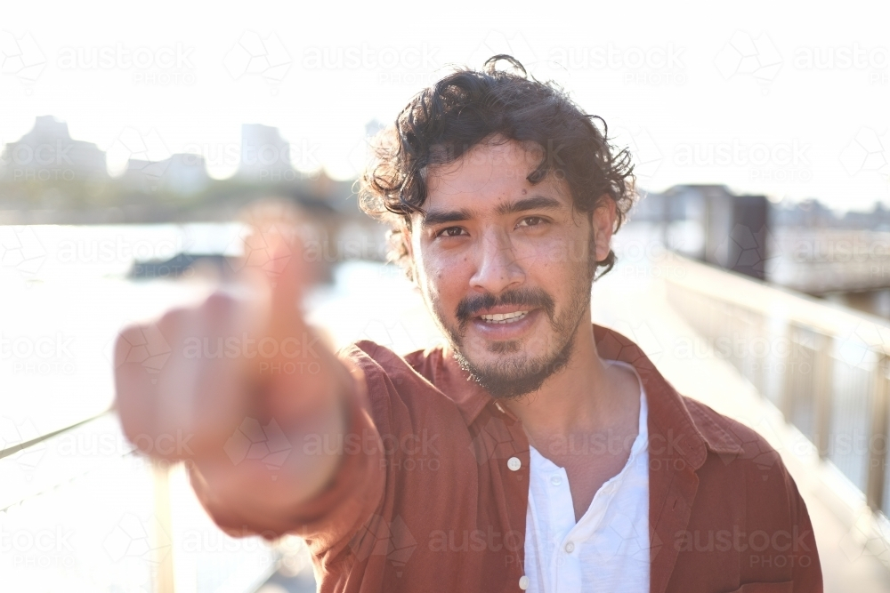 Smiling curly haired man pointing with his index finger - Australian Stock Image
