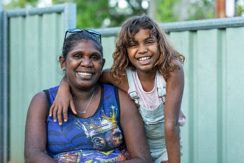 Smiling daughter draping arm around mother's neck outside - Australian Stock Image