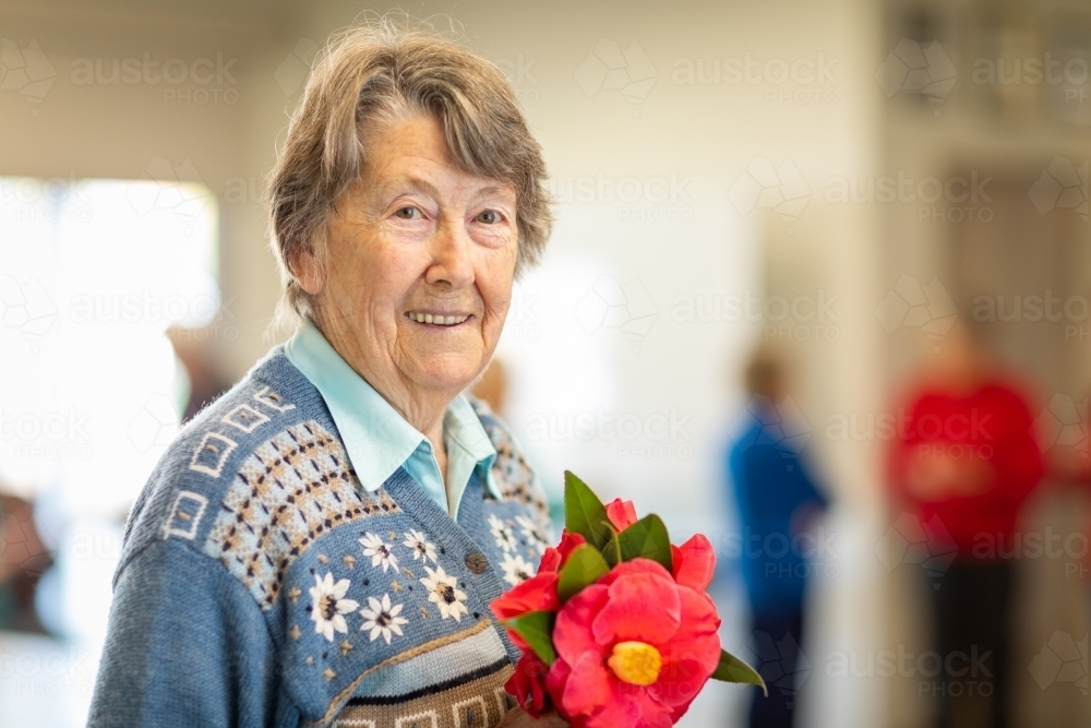 smiling elderly woman holding camellia flowers - Australian Stock Image