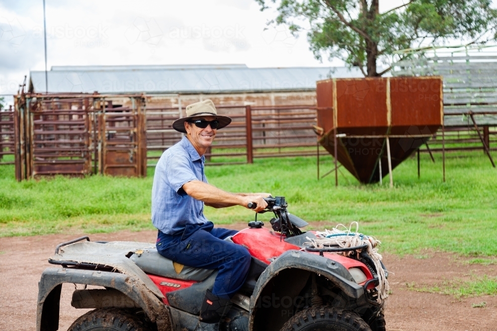 Smiling farmer on quad bike with hat and sunglasses - Australian Stock Image
