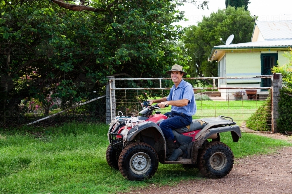 Smiling farmer sitting on quad bike outside his front gate - Australian Stock Image