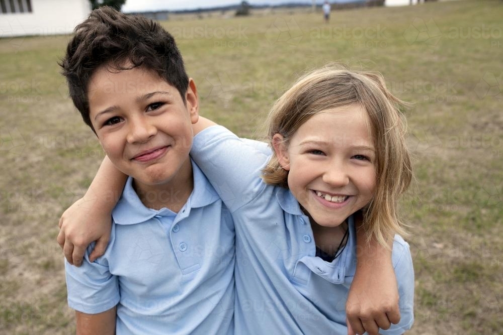 Smiling girl and boy wearing school uniform with arm around each other - Australian Stock Image