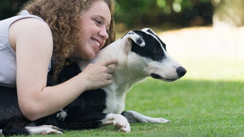Smiling girl laying on grass with her dog - Australian Stock Image