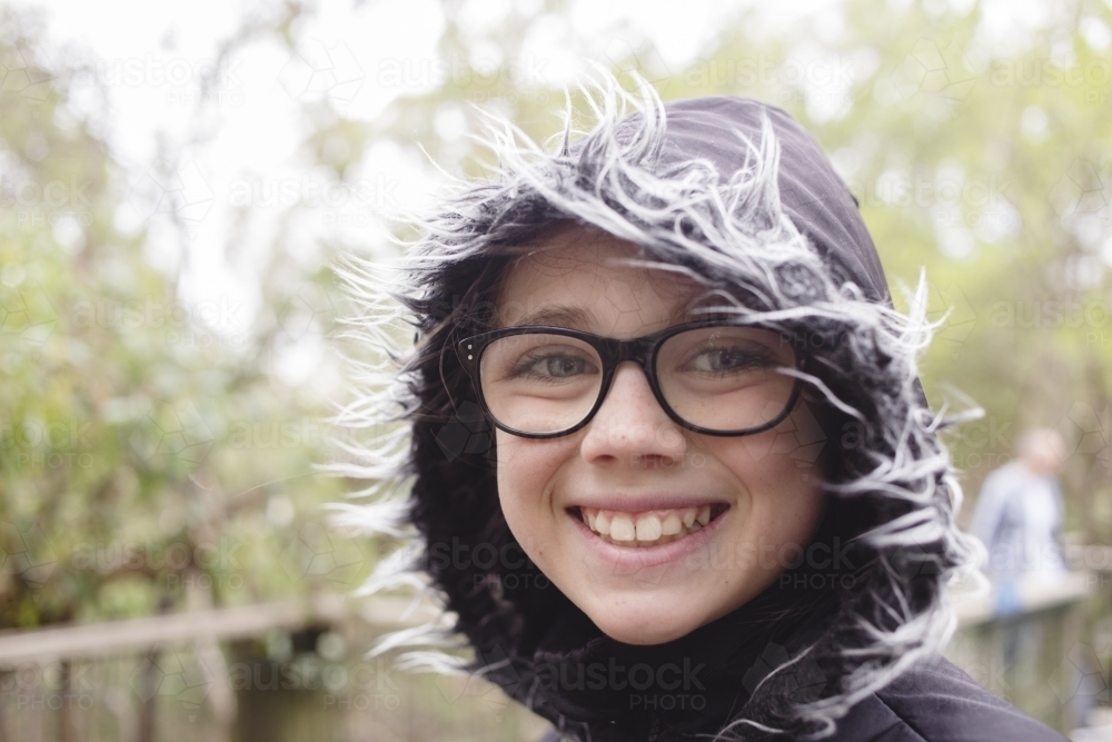 Smiling girl outdoors wearing hooded jacket - Australian Stock Image