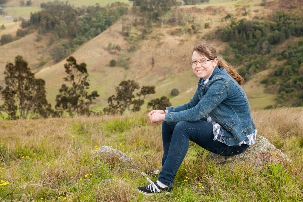 Smiling girl sitting on a rock in the hills - Australian Stock Image