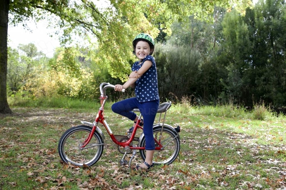 Smiling girl wearing helmet with red bike - Australian Stock Image