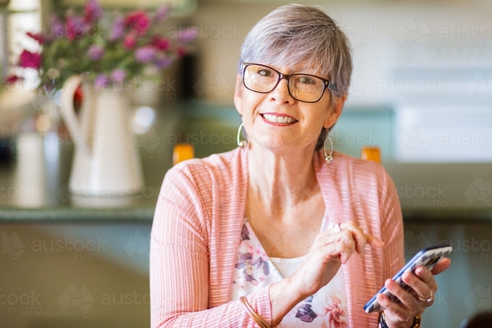 Smiling happy middle aged woman texting on phone - Australian Stock Image