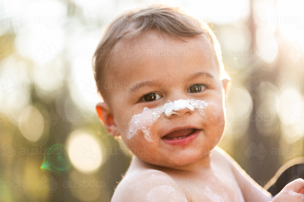 Smiling happy portrait of young Aboriginal toddler boy in ochre paint outdoors  - Australian Stock Image