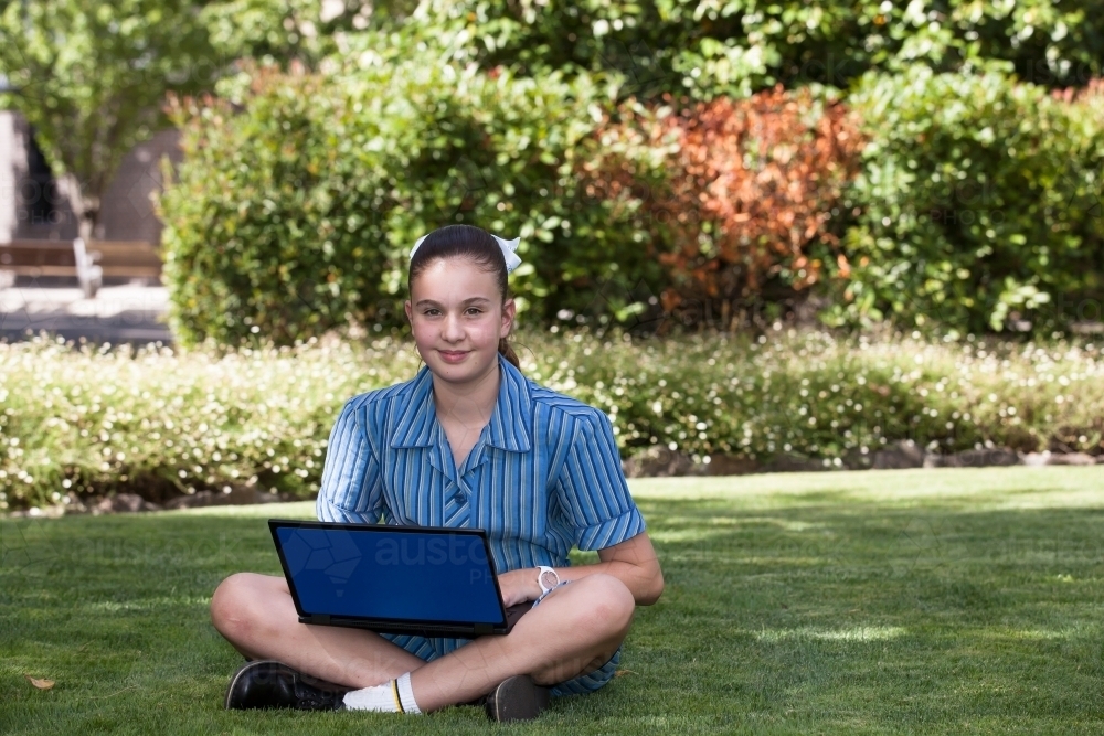 Smiling high school student working on a laptop in gardens - Australian Stock Image