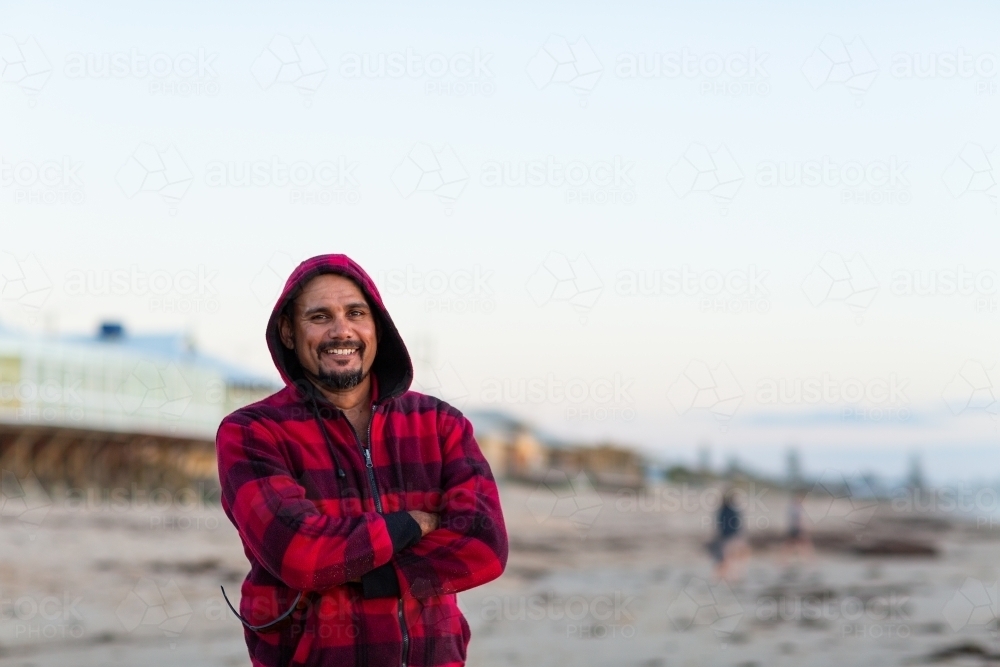 Smiling indigenous man standing with arms crossed in red checked hoody - Australian Stock Image
