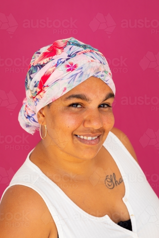 smiling indigenous woman wearing floral head wrap against pink background - Australian Stock Image