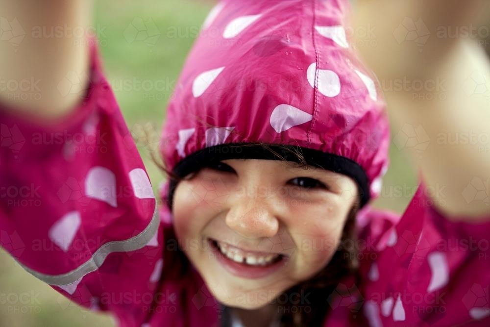 Smiling laughing girl wearing pink raincoat - Australian Stock Image