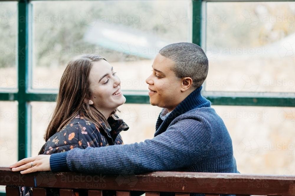 smiling lgbtqi couple looking at each other sitting on a bench - Australian Stock Image