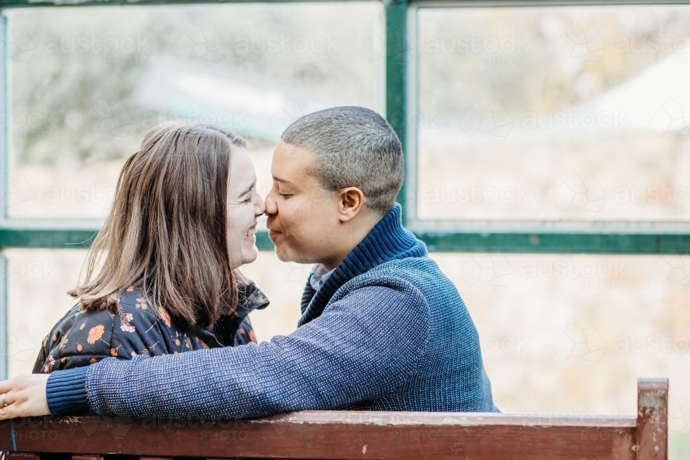smiling lgbtqi couple about to kiss while sitting on a bench - Australian Stock Image