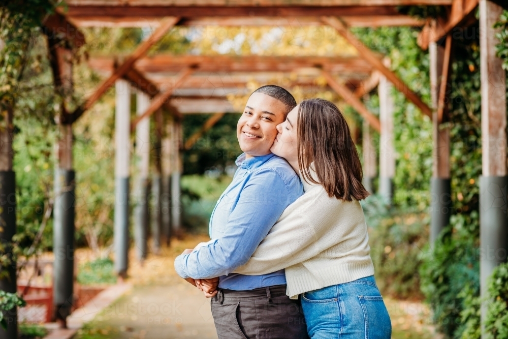 smiling lgbtqi couple hugging and kissing on the cheek - Australian Stock Image