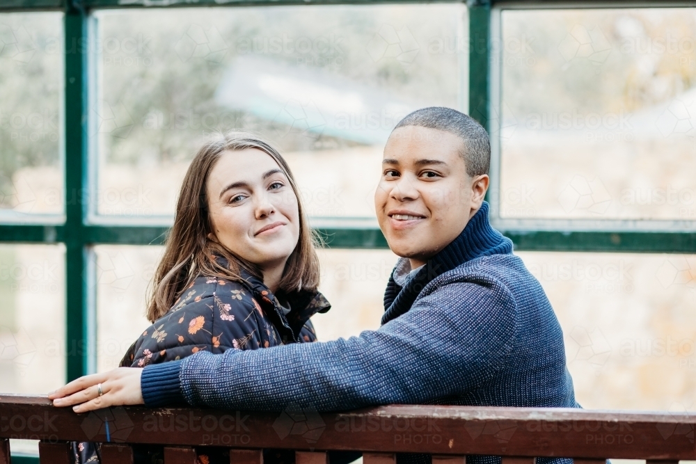 smiling lgbtqi couple sitting on a bench - Australian Stock Image