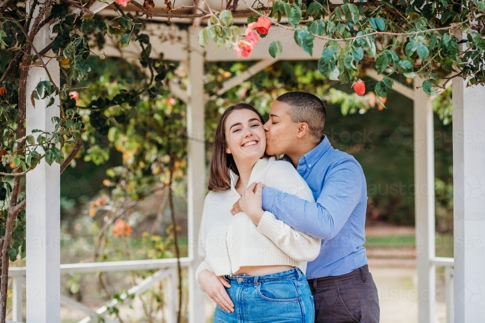 smiling lgbtqi couple with one kissing the other on her cheek - Australian Stock Image