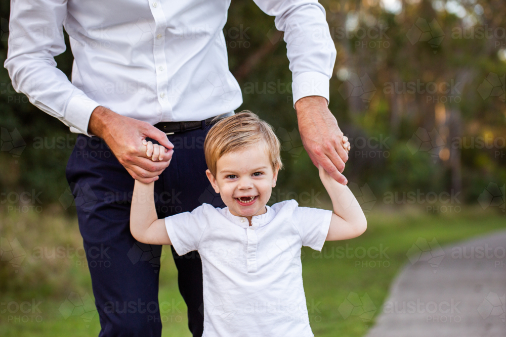 Image of Smiling little boy holding his dads hands walking along path ...