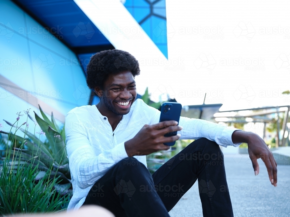 Image of Smiling man in front of a blue building using a phone ...