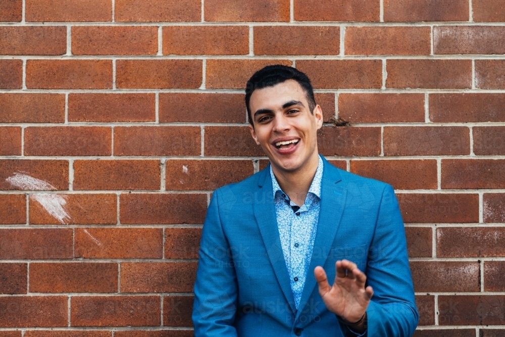 smiling man leaning against brick wall - Australian Stock Image