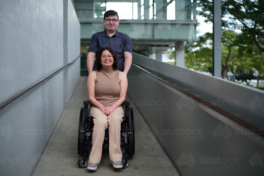 Smiling man standing behind the woman with a disabilityoutdoors - Australian Stock Image