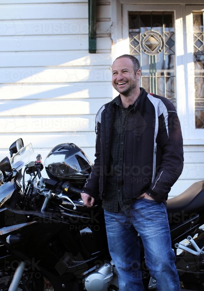 Smiling man standing in front of his motorbike - Australian Stock Image