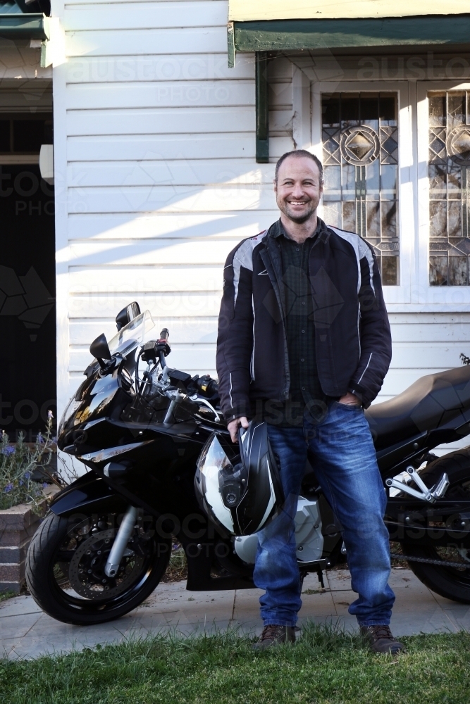 Smiling man standing in front of his motorbike - Australian Stock Image