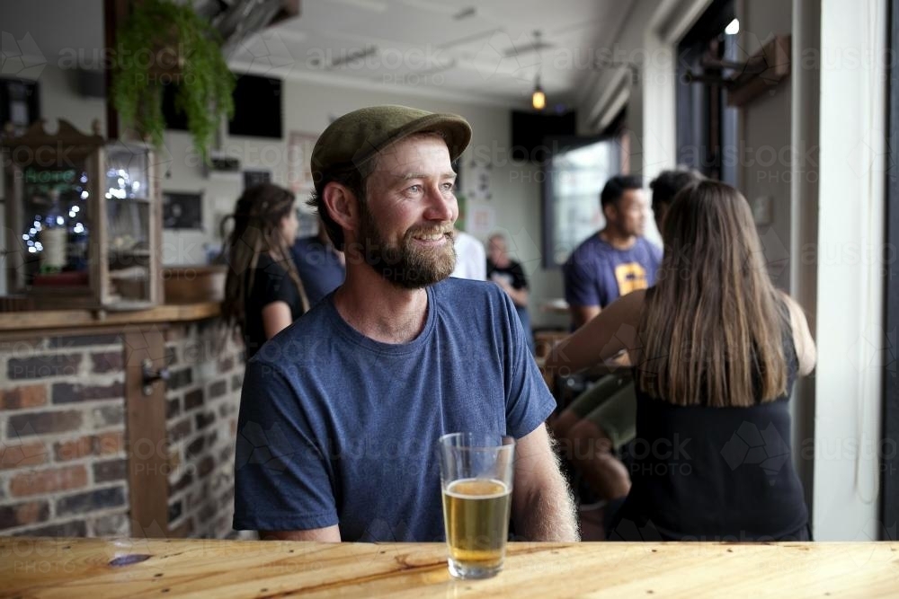 Smiling man wearing hat having a drink at craft beer bar - Australian Stock Image