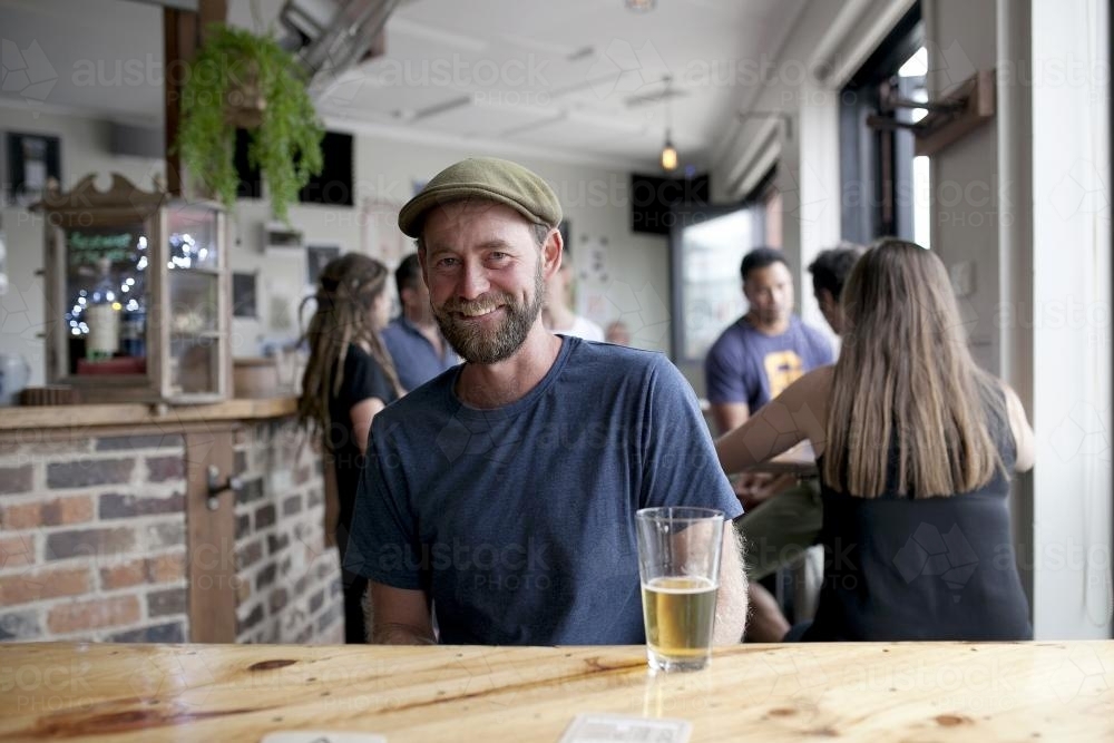 Smiling man wearing hat having a drink at craft beer bar - Australian Stock Image