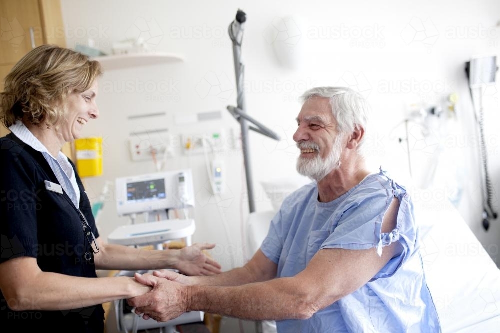 Smiling middle aged male patient shaking hands with a nurse in a hospital ward - Australian Stock Image