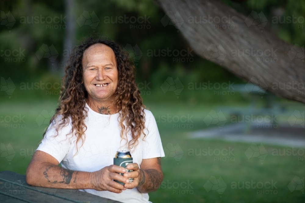 smiling middle-aged man holding drink outdoors in park - Australian Stock Image